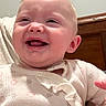 Embreigh is registered to the contest to win money with this photo: baby, child, smiling, laughing, onesie, hair, face, skin, person, indoor, bedroom, wood, tattoo, arm, happy, infant, cute, expression, portrait, clothing