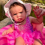 Athena joined the competition — help win amazing prizes! baby, child, toddler, swimsuit, pink, sunhat, inflatable, pool_float, water, outdoor, nature, trees, summer, hand, face, expression, sunlight, shadow, cute, sitting