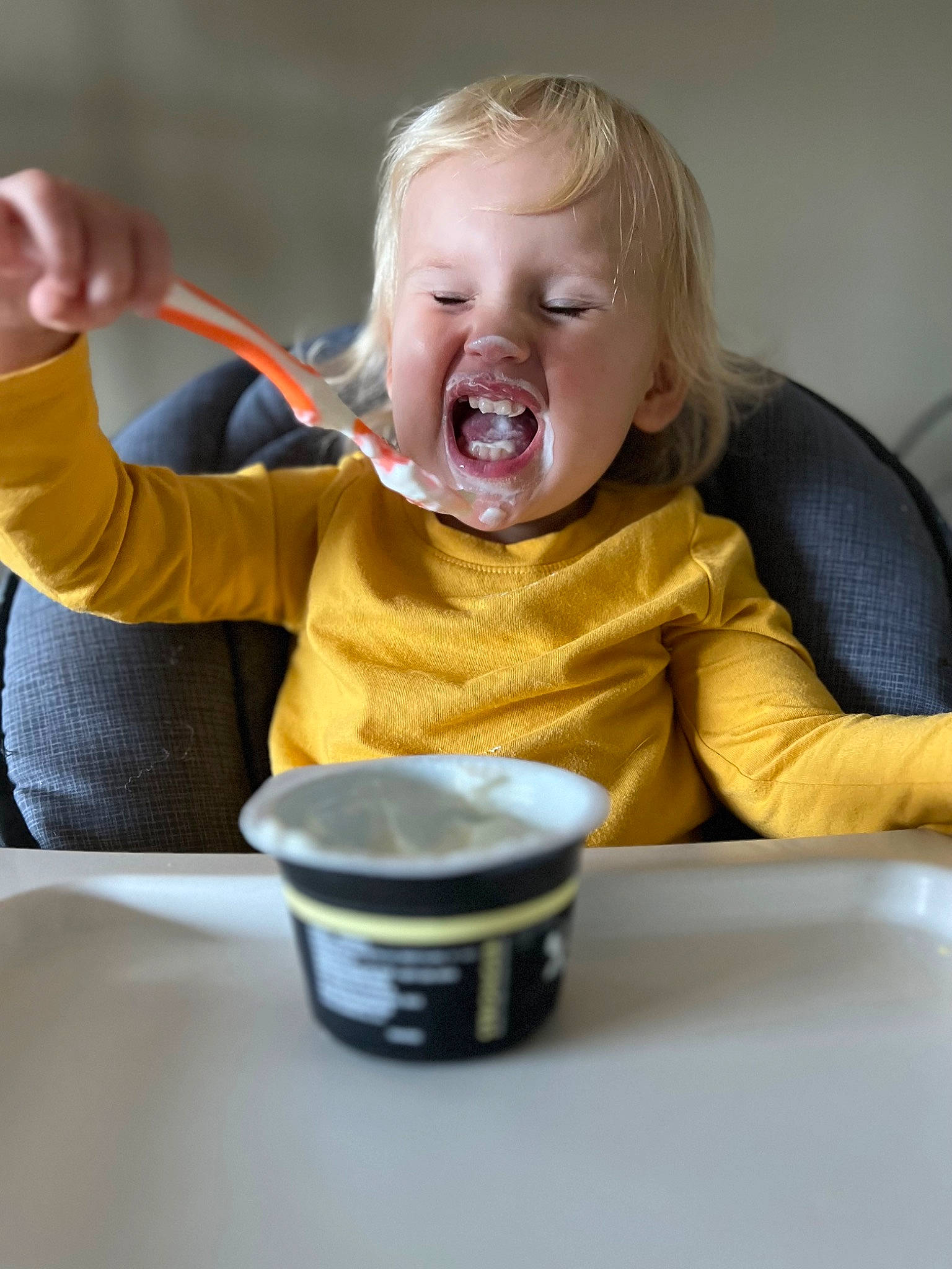 Lylah is registered to the contest to win money with this photo: arm, baby, baby_food, breakfast, chair, child, comfort_food, cup, drinkware, eating, food_craving, fun, happy, mouth, person, room, sitting, smile, table, tableware