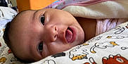 Evangeline is registered to the contest to win money with this photo: baby, close_up, face, tongue, blanket, cartoon, cat_pattern, infant, cute, lying_down, bed, soft, skin, eyes, clothing, pink, white, comfort, indoors, child