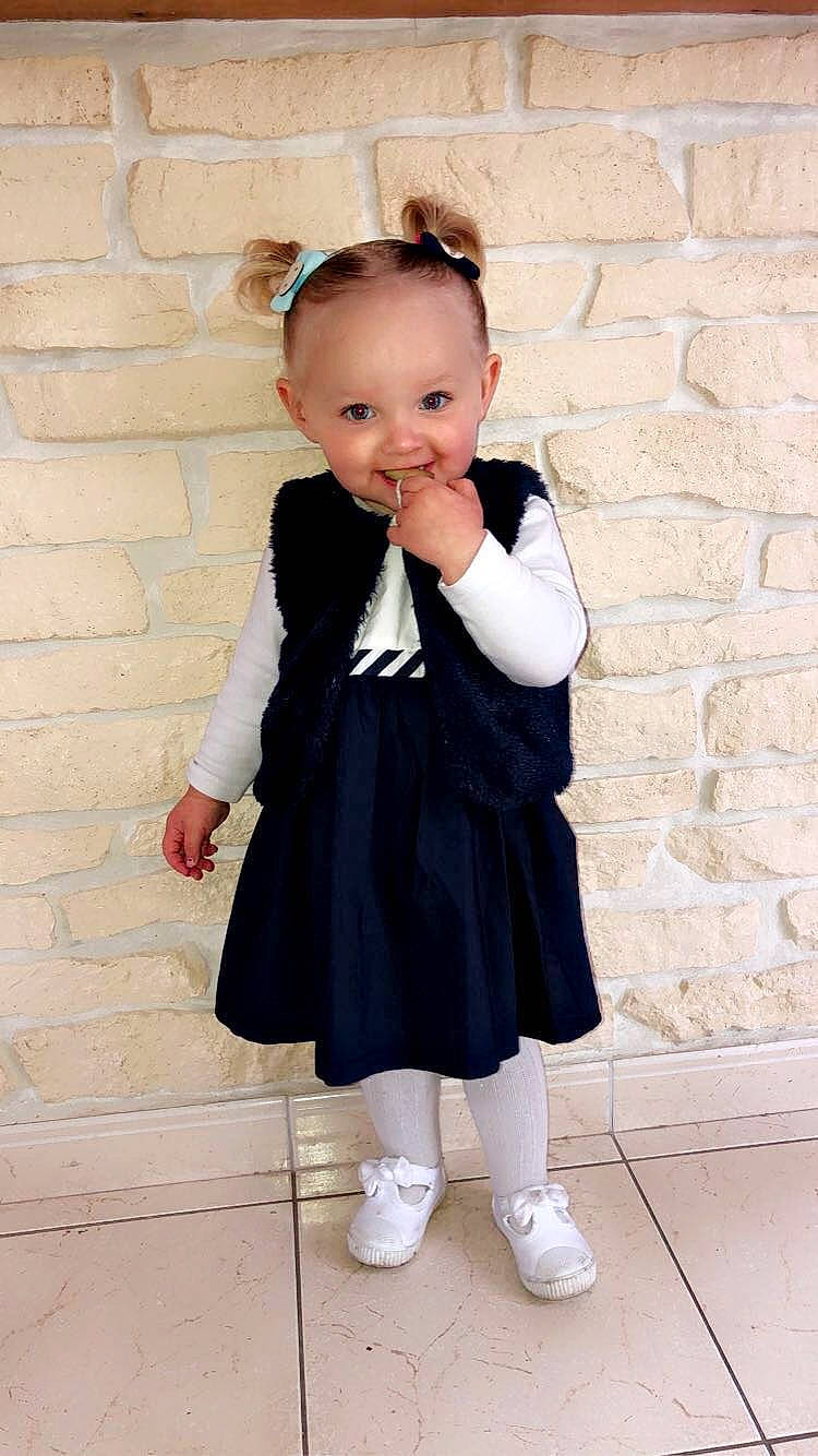 Elyana participe au concours pour gagner de l'argent avec cette photo : baby_toddler_clothing, clothing, collar, day_dress, face, flash_photography, gesture, hair, hand, happy, human_body, joint, joy, leg, outerwear, person, pink, shoulder, sleeve, standing