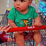 toddler, child, shopping_cart, grocery_store, green_shirt, giraffe_print, curly_hair, blue_bow, colorful_sandals, hand, aisle, shelves, baby_products, diapers, floor, person, cute, expression, indoor, retail
