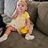 baby, child, yellow_dress, headband, pacifier, rubber_duck, couch, gray_couch, socks, indoor, bookshelf, books, furniture, sitting, cute, infant, person, home, toy, soft_lighting
