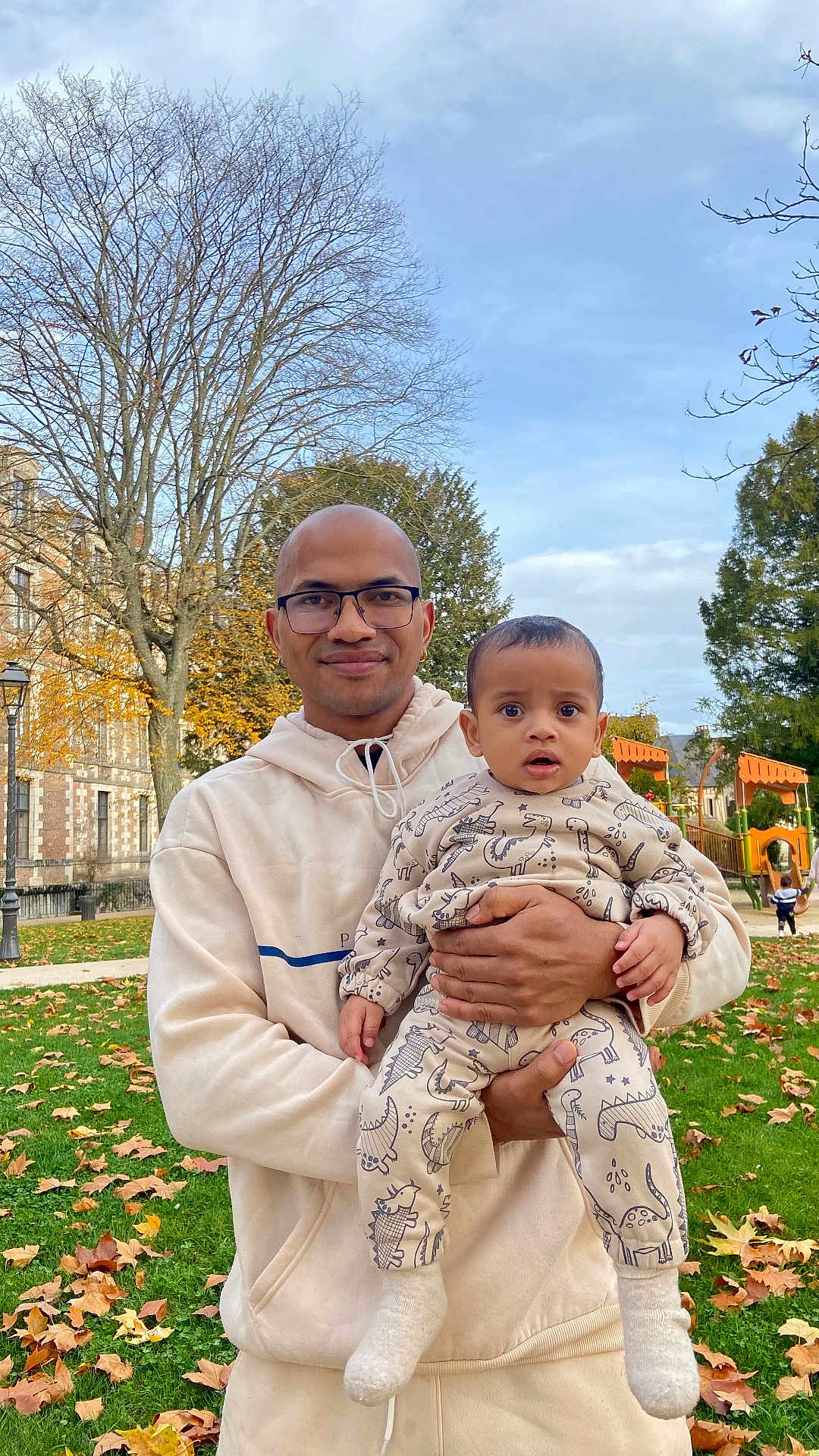 Brandon participe au concours pour gagner de l'argent avec cette photo : man, baby, child, glasses, hoodie, dinosaur_pattern, outdoor, park, grass, leaves, autumn, trees, playground, socks, holding, smiling, daytime, person, nature, casual_clothing