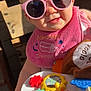 accessory, baby, child, closeup, clothing, colorful, cute, face, hand, happy, indoor, infant, person, pink_bib, playful, seat, smile, sunglasses, sunlight, toy