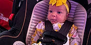 Serenity is registered to the contest to win money with this photo: baby, infant, car_seat, yellow_bow, sunflower_pattern, onesie, child, face, seatbelt, straps, clothing, indoor, purple_light, headband, cute, sitting, young_child, person, portrait, newborn