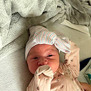 Emmalyn is registered to the contest to win money with this photo: baby, newborn, infant, hat, bow, onesie, floral_pattern, blanket, soft_texture, hand, face, lying_down, cute, indoors, sleepwear, closeup, person, skin, headwear, cozy