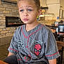 child, boy, blue_eyes, spiderman, jersey, restaurant, table, chair, indoor, casual_clothing, face, expression, messy_face, short_hair, person, seated, background, wall_art, clock, lighting