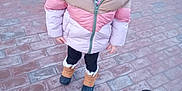 Rhea is registered to the contest to win money with this photo: child, girl, winter_jacket, hat, pom_pom, smile, outdoor, brick_path, footwear, boots, black_pants, wheelchair, concrete, pavement, cold_weather, cute, standing, person, young, casual_clothing