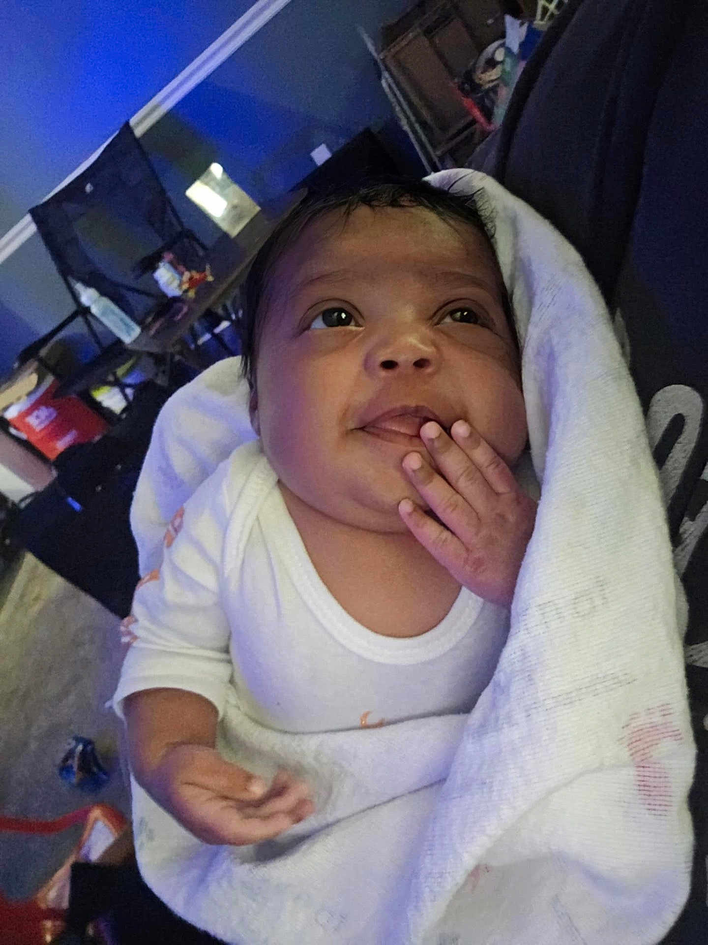 Journey is registered to the contest to win money with this photo: baby, infant, blanket, white_clothing, hand, face, indoors, person, curious, wrapped, young_child, sleepwear, toddler, skin, portrait, expression, sitting, cozy, soft_light, home