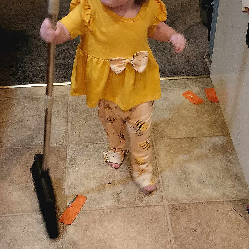 Alysia is registered to the contest to win money with this photo: child, toddler, broom, floor, tile_floor, yellow_clothing, indoor, kitchen, cleaning, person, carpet, cabinet, door, toy, home, pants, footwear, hair, cute, activity