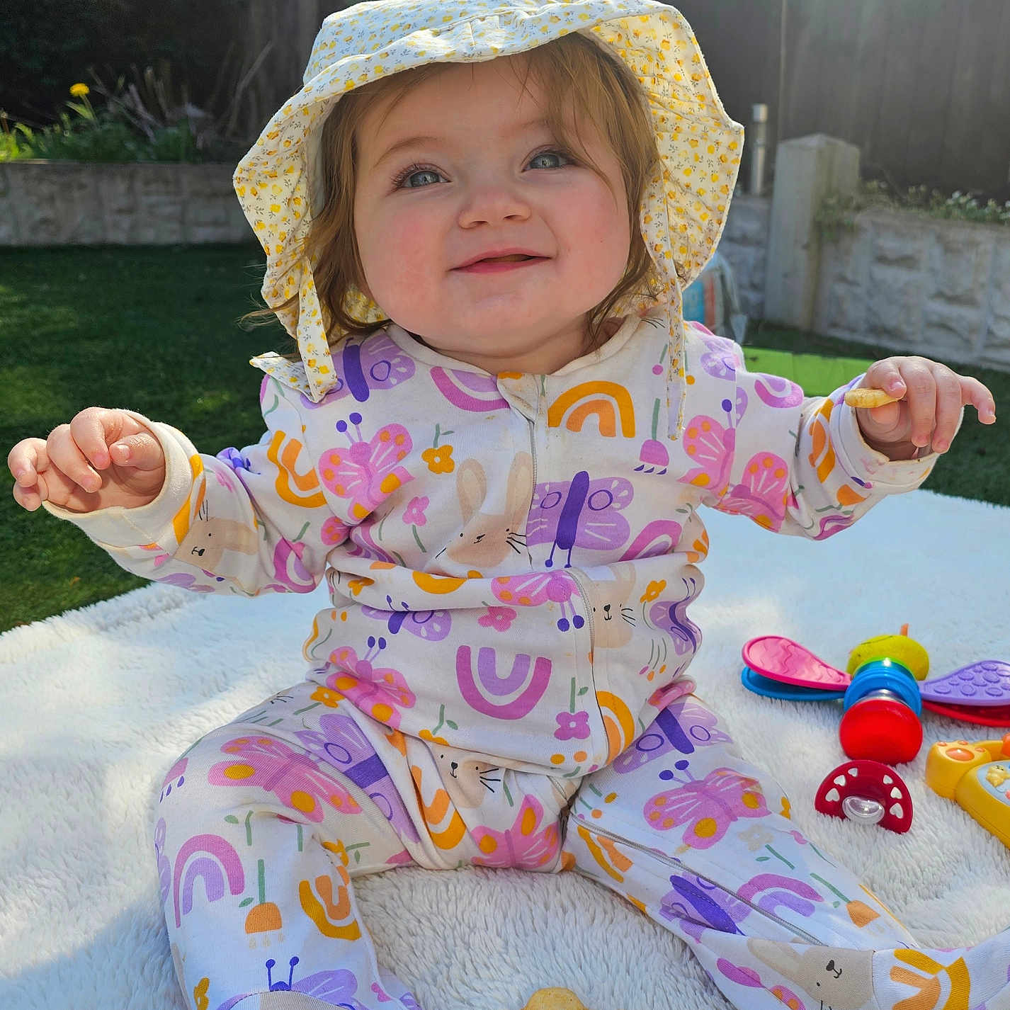 Luna is registered to the contest to win money with this photo: baby, bodypart, bonnet, cap, clothing, face, finger, grass, hand, hat, head, outdoors, pajamas, person, photography, plant, portrait, sitting, summer, sunhat