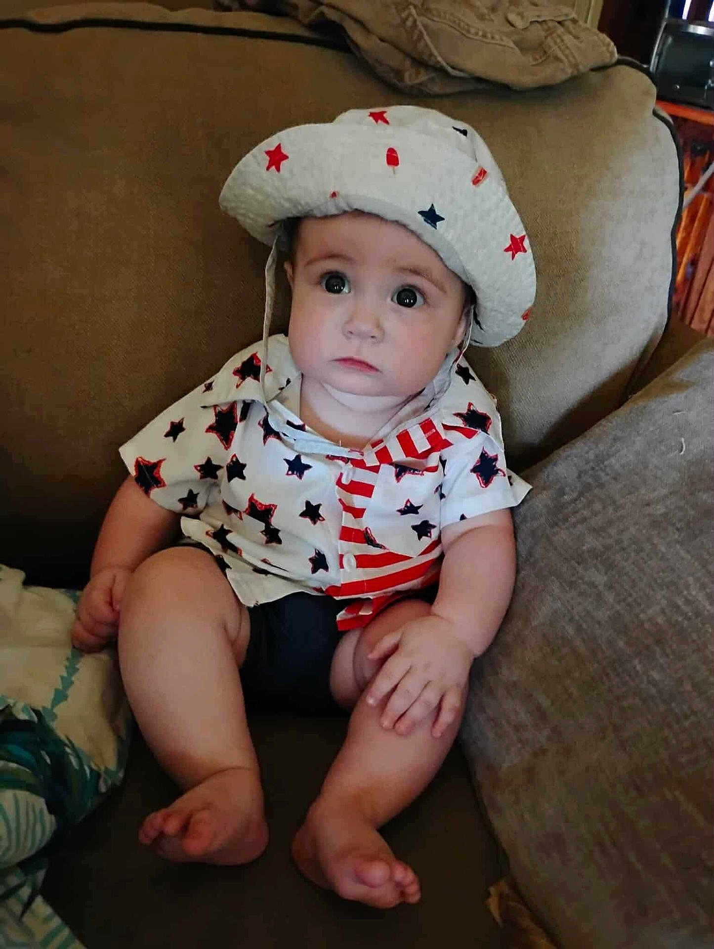 Elijah is registered to the contest to win money with this photo: baby, child, infant, couch, hat, clothing, stars, stripes, sitting, indoors, cute, portrait, face, hand, foot, furniture, expression, young, person, apparel