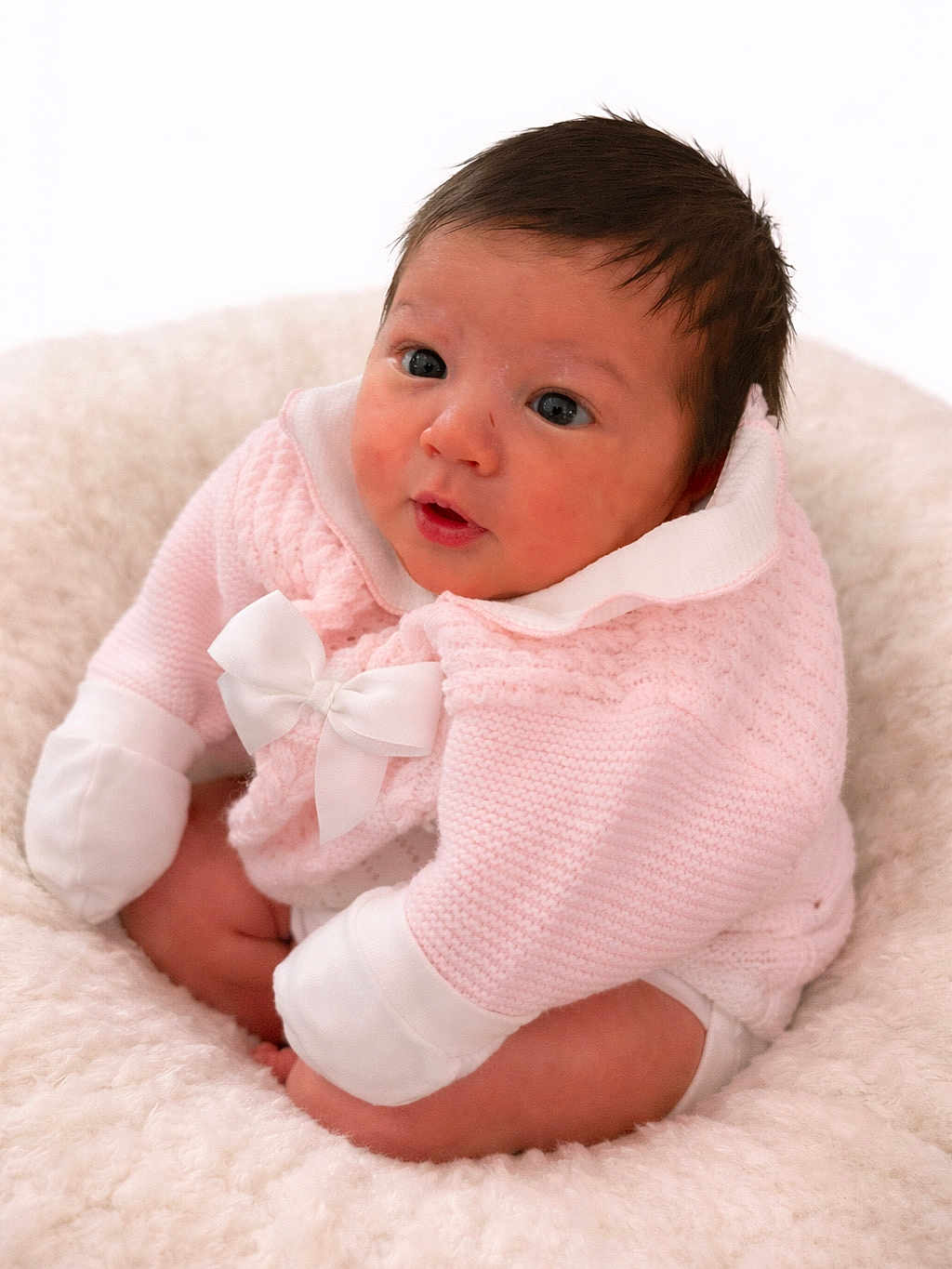 Vienna is registered to the contest to win money with this photo: baby, infant, pink_clothing, white_bow, knitwear, fluffy_blanket, cute, portrait, child, sitting, soft_texture, indoor, young, adorable, face, expression, curious, cozy, warm, small