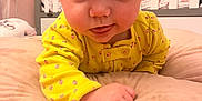 Isabella is registered to the contest to win money with this photo: baby, child, infant, yellow_clothing, headband, bow, tongue_out, cushion, crib, nursery, bedroom, soft_toys, cute, indoors, person, smiling, happy, face, lying_down, closeup