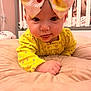 baby, child, infant, yellow_clothing, headband, bow, tongue_out, cushion, crib, nursery, bedroom, soft_toys, cute, indoors, person, smiling, happy, face, lying_down, closeup