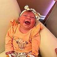 Isabella joined the competition — help win amazing prizes! baby, smiling, infant, headband, orange_clothing, sitting, couch, indoor, happy, portrait, child, cute, apparel, patterned_pants, flower, furniture, skin, tongue_out, head, person