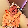 baby, smiling, infant, headband, orange_clothing, sitting, couch, indoor, happy, portrait, child, cute, apparel, patterned_pants, flower, furniture, skin, tongue_out, head, person
