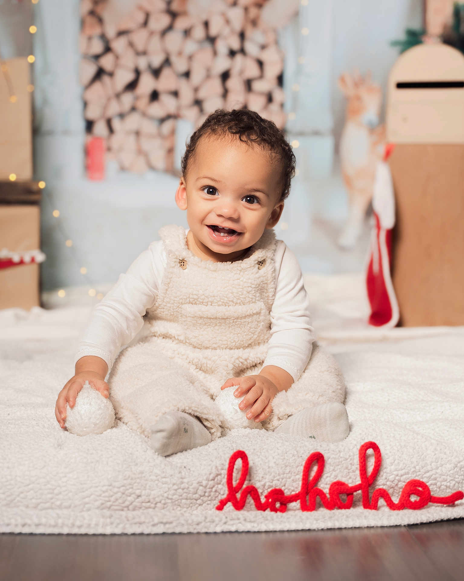 Swann participe au concours pour gagner de l'argent avec cette photo : toddler, baby, child, smiling, sitting, white_clothing, cozy, blanket, holiday_decor, firewood, indoors, soft_toys, festive, christmas, red_text, floor, cute, happy, portrait, warm_lighting