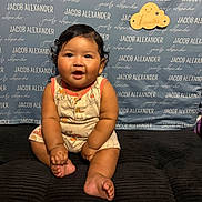Jacob joined the competition — help win amazing prizes! baby, infant, child, sitting, romper, curly_hair, smiling, indoor, cushion, background, sign, text, name, portrait, cute, chubby, happy, skin, feet, hands