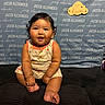 baby, infant, child, sitting, romper, curly_hair, smiling, indoor, cushion, background, sign, text, name, portrait, cute, chubby, happy, skin, feet, hands
