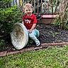 Brodhi is registered to the contest to win money with this photo: toddler, child, red_shirt, mamas_boy, garden, flowers, grass, birdbath, decorative_stone, outdoor, smiling, greenery, plants, brick_border, deck, wooden_railing, playful, cute, young_child, daylight