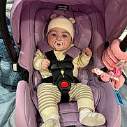 Camille is registered to the contest to win money with this photo: baby, infant, car_seat, pacifier, knit_hat, knitwear, purple, seatbelt, toy, plush, blanket, clothing, child, indoor, cute, person, sitting, face, headwear, comfort