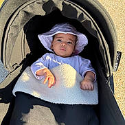 Celia participe au concours pour gagner de l'argent avec cette photo : baby, stroller, hat, blanket, outdoor, sunlight, infant, child, person, clothing, face, hand, headwear, baby_carriage, shadow, gravel, relaxing, cute, young_child, portrait