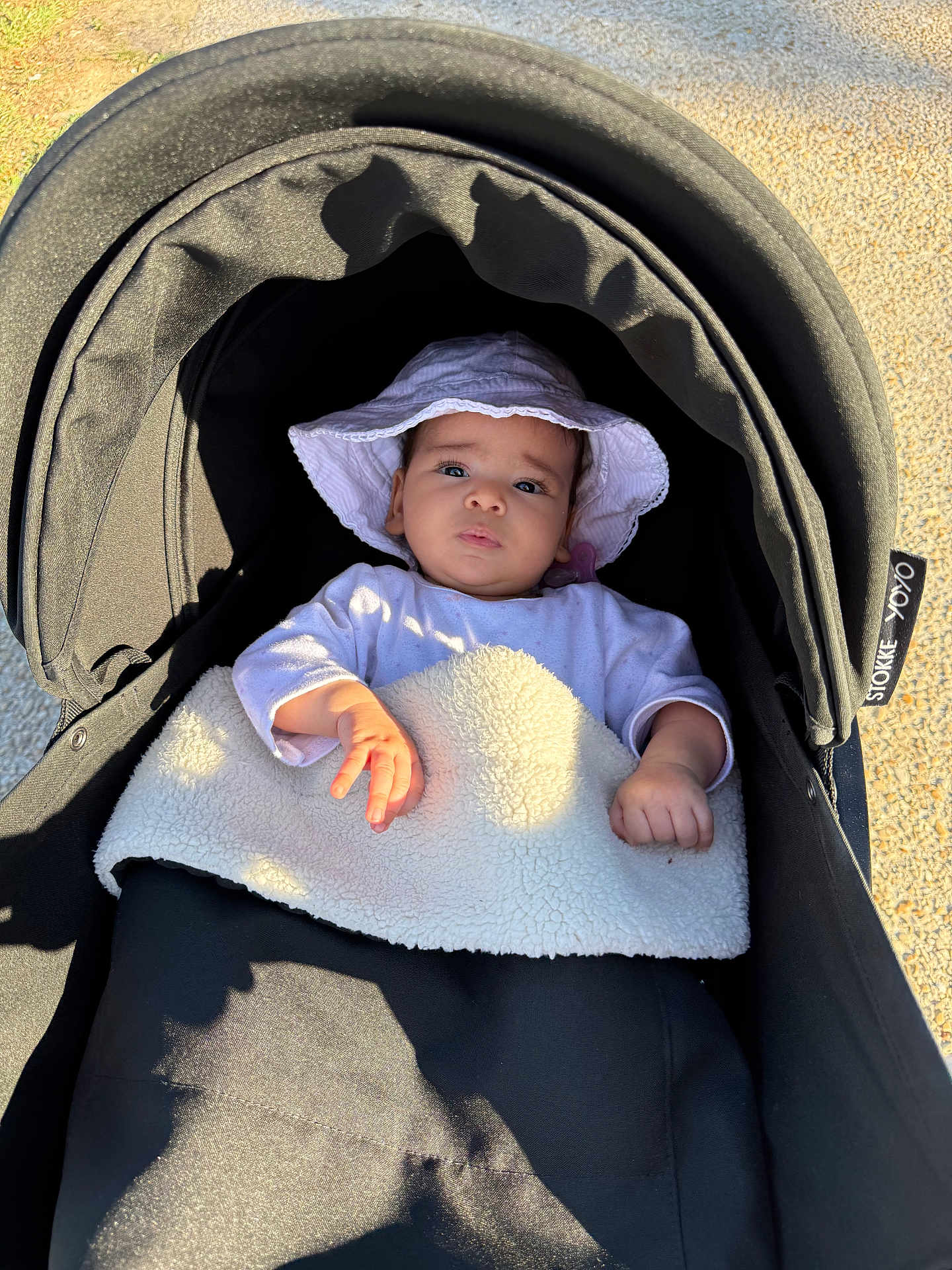 Celia participe au concours pour gagner de l'argent avec cette photo : baby, stroller, hat, blanket, outdoor, sunlight, infant, child, person, clothing, face, hand, headwear, baby_carriage, shadow, gravel, relaxing, cute, young_child, portrait