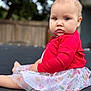 Lyla joined the competition — help win amazing prizes! baby, casual_clothing, child, colorful_skirt, curious_look, cute, daylight, expression, face, fence, greenery, hearts_pattern, human, infant, outdoor, portrait, red_sweater, sitting, soft_lighting, young_child
