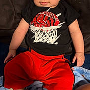 Dominic is registered to the contest to win money with this photo: baby, child, infant, portrait, sitting, smiling, wide_eyed, basketball, sportswear, black_shirt, red_pants, sneakers, shoes, couch, blanket, indoor, home, face, clothing, photograph