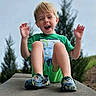 child, boy, green_shirt, shorts, outdoor, happy, laughing, sitting, concrete, shoes, trees, nature, casual, daylight, playful, portrait, smile, grass, fun, youth