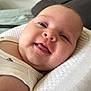 baby, smiling, close_up, infant, face, tongue, cute, white_pillow, quilted, skin, child, happy, lying_down, indoors, soft_light, apparel, sleeveless_shirt, head, young, portrait