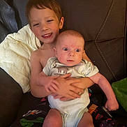 Nathaniel joined the competition — help win amazing prizes! baby, child, sibling, couch, smile, holding, indoor, face, happy, person, clothing, blanket, expression, cute, seated, infant, pajamas, family, young_child, portrait