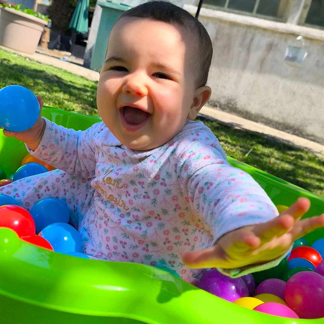 Esmée a rejoint le concours — aidez-le/la à gagner de superbes lots ! baby, ball_pit, child, colorful_balls, cute, daylight, grass, green, greenery, happy, infant, joy, outdoor, person, plastic, play, reaching, smiling, sunlight, toy