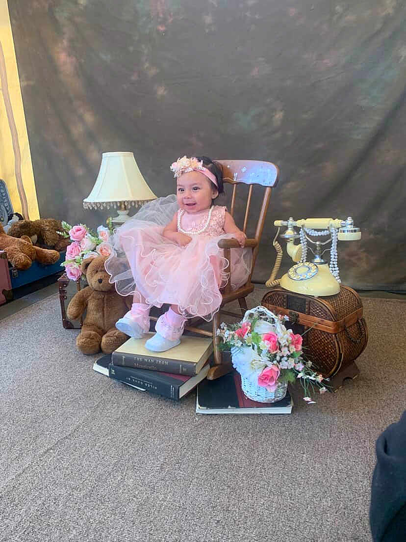 Jewells is registered to the contest to win money with this photo: toddler, child, pink_dress, headband, wooden_chair, books, teddy_bear, lamp, rotary_phone, basket, flowers, carpet, vintage, smile, indoor, portrait, decor, cute, happy, girl