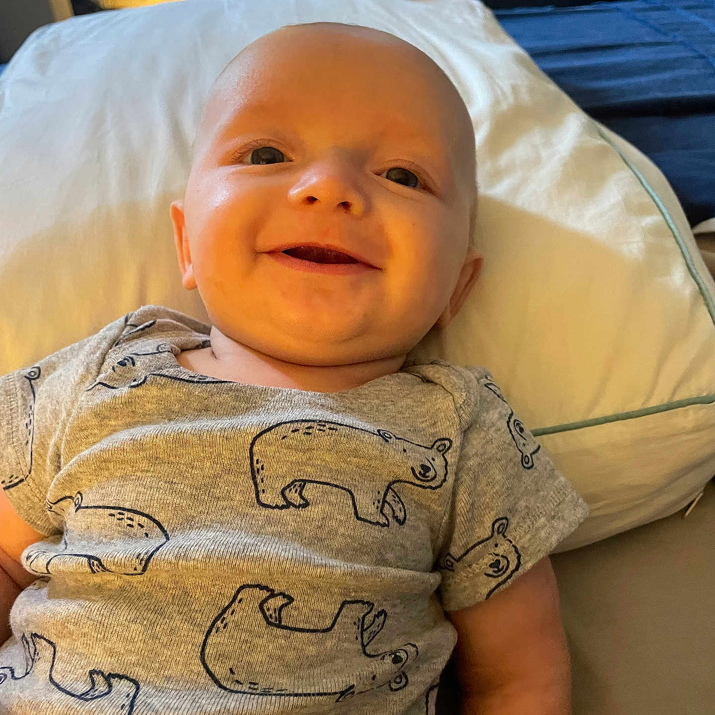 Jhett is registered to the contest to win money with this photo: arm, baby, bear_pattern, bedroom, child, clothing, cute, happy, head, indoors, infant, lying_down, onesie, person, pillow, portrait, skin, smiling, soft_lighting, toddler