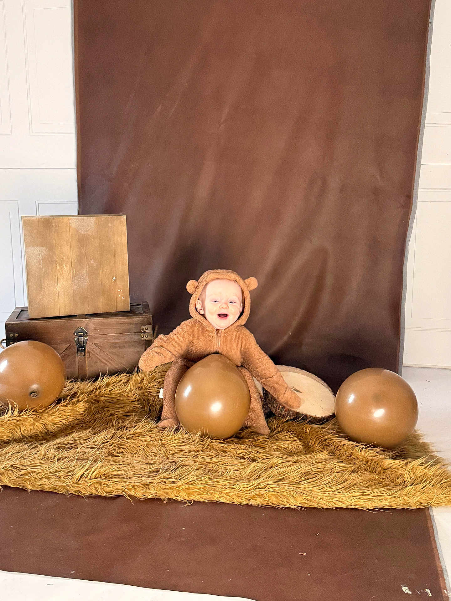 Emory is registered to the contest to win money with this photo: baby, child, costume, bear, brown, balloon, rug, fur, wood, box, happy, smiling, indoor, portrait, cute, plush, sitting, background, photography, cozy