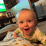 Emory is registered to the contest to win money with this photo: baby, infant, smile, joyful, crawling, pajamas, dinosaur_print, blanket, living_room, carpet, furniture, television, photo_frame, curtains, home_interior, child, person, face, head, happy
