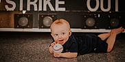 Emory is registered to the contest to win money with this photo: baby, baseball, child, floor, black_clothing, tongue_out, happy, indoor, sports, playful, portrait, crawling, young_child, smiling, person, head, face, short_hair, light_skin, toy