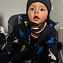 Sun participe au concours pour gagner de l'argent avec cette photo : baby, child, toddler, face, blue_eyes, hat, beanie, jacket, dinosaur_pattern, scarf, winter_clothing, sitting, indoor, chair, expression, cute, clothing, person, portrait, warm