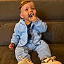 baby, child, pacifier, sitting, blue_clothing, sneakers, couch, indoor, happy, cute, face, hand, footwear, hoodie, pants, person, infant, smiling, casual_clothing, small_child