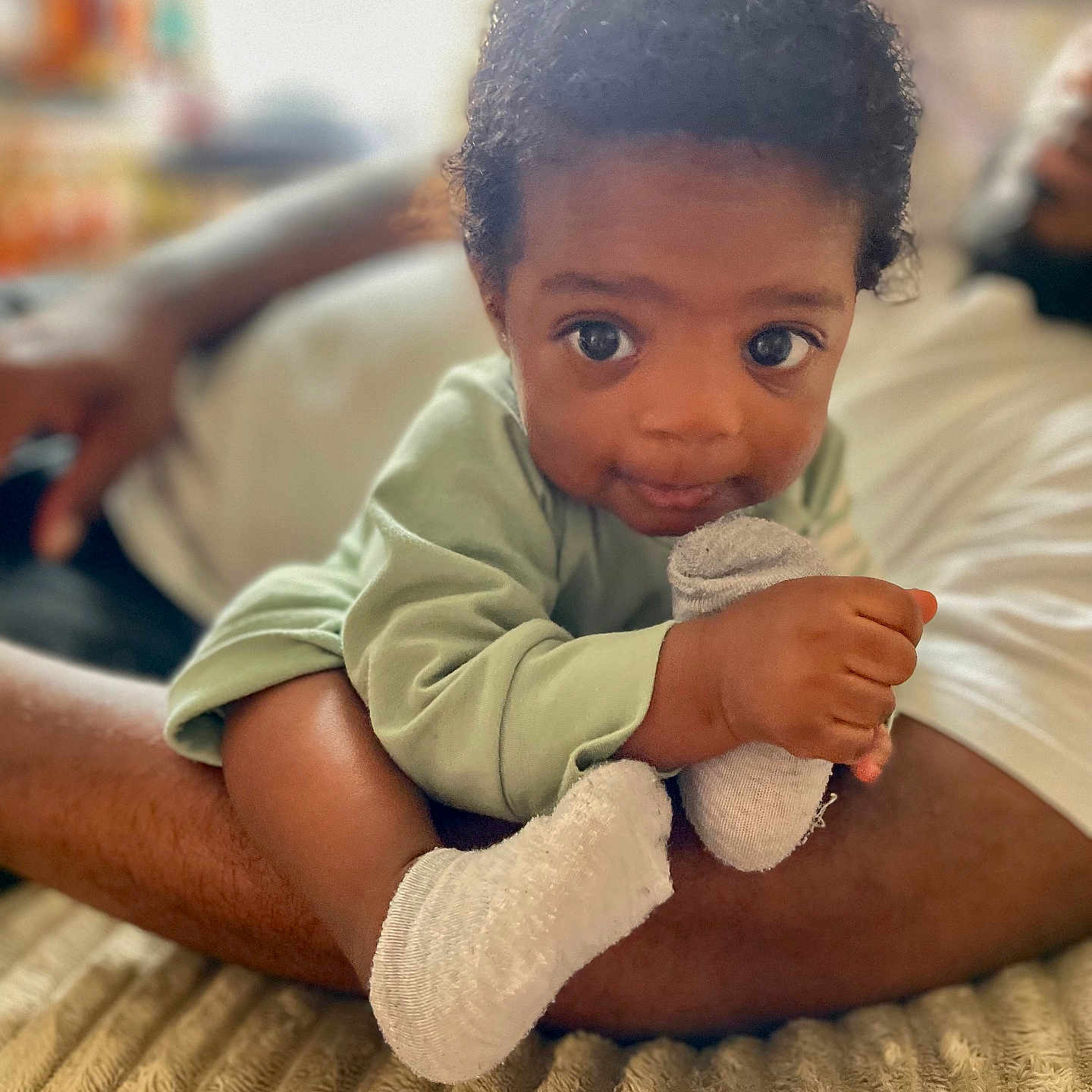 Sire joined the competition — help win amazing prizes! baby, child, infant, person, face, hand, sock, footwear, curly_hair, lying_down, arm, adult, indoor, blanket, green_clothing, skin, closeup, candid, cozy, soft_light