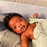 Sire is registered to the contest to win money with this photo: baby, infant, child, blanket, crib, smiling, face, skin, arm, curly_hair, indoors, bed, comfort, expression, cute, portrait, young, resting, wrapped, greeting