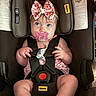 baby, infant, car_seat, pacifier, bow, child, safety_harness, cute, pink, wide_eyes, chubby_cheeks, seatbelt, face, person, indoor, clothing, headband, expression, sitting, closeup