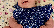 Millie is registered to the contest to win money with this photo: baby, infant, smile, blue_dress, headband, lying_down, patterned_blanket, happy, cute, child, small_hands, small_feet, face, person, indoors, colorful, floral, soft, portrait, young