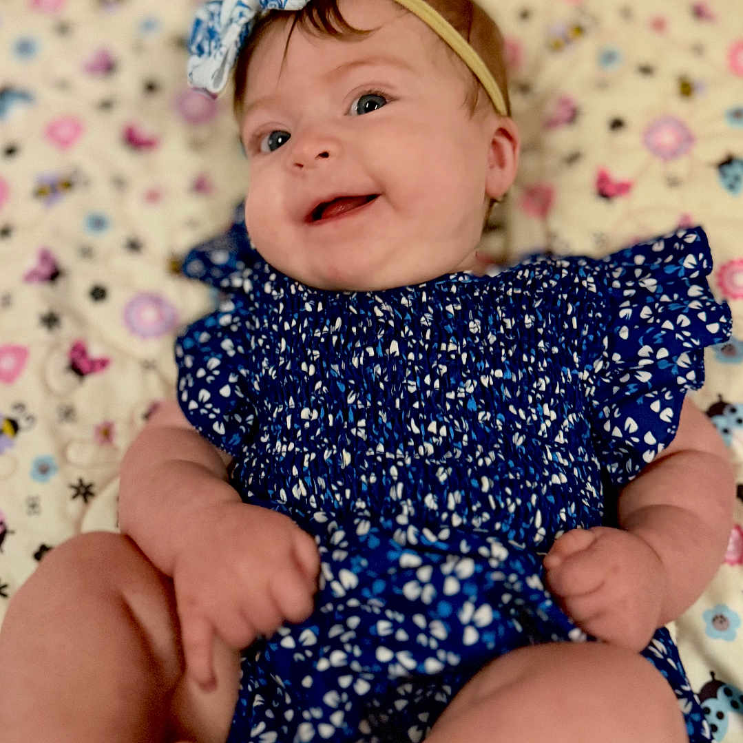 Millie is registered to the contest to win money with this photo: baby, smiling, blue_outfit, headband, patterned_blanket, infant, cute, happy, lying_down, child, soft_lighting, portrait, closeup, skin, bare_feet, chubby_arms, adorable, indoor, colorful, playful