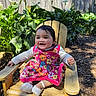 Charlotte is registered to the contest to win money with this photo: baby, child, smiling, outdoor, wooden_chair, flower_dress, plants, greenery, sunlight, fence, happy, cute, sitting, feet, sock, nature, portrait, garden, daylight, person
