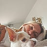 dog, woman, pet, companion, portrait, cuddle, bed, blanket, indoors, home, cozy, white_dog, pointy_ears, chihuahua, human, face, blonde_hair, tattoo, soft_lighting, relaxed