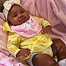baby, blanket, bow, cheeks, couch, cute, footwear, hand, happy, headband, indoor, infant, lying_down, pink_bib, relaxing, skin, smile, soft_texture, toddler, yellow_clothing